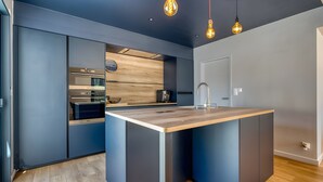 A modern kitchen with a central island, built-in appliances, and pendant lighting. - La Villa des Pins d'Or – Family Villa with Pool and Spa in a Peaceful Natural Setting (La Tranche-sur-Mer)