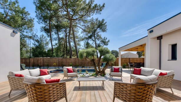 A deck with wicker furniture and a central table, surrounded by trees and a wooden fence. - La Villa des Pins d'Or – Family Villa with Pool and Spa in a Peaceful Natural Setting (La Tranche-sur-Mer)