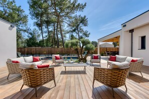 Une terrasse dotée de meubles en osier et d’une table centrale, entourée d’arbres et d’une clôture en bois.