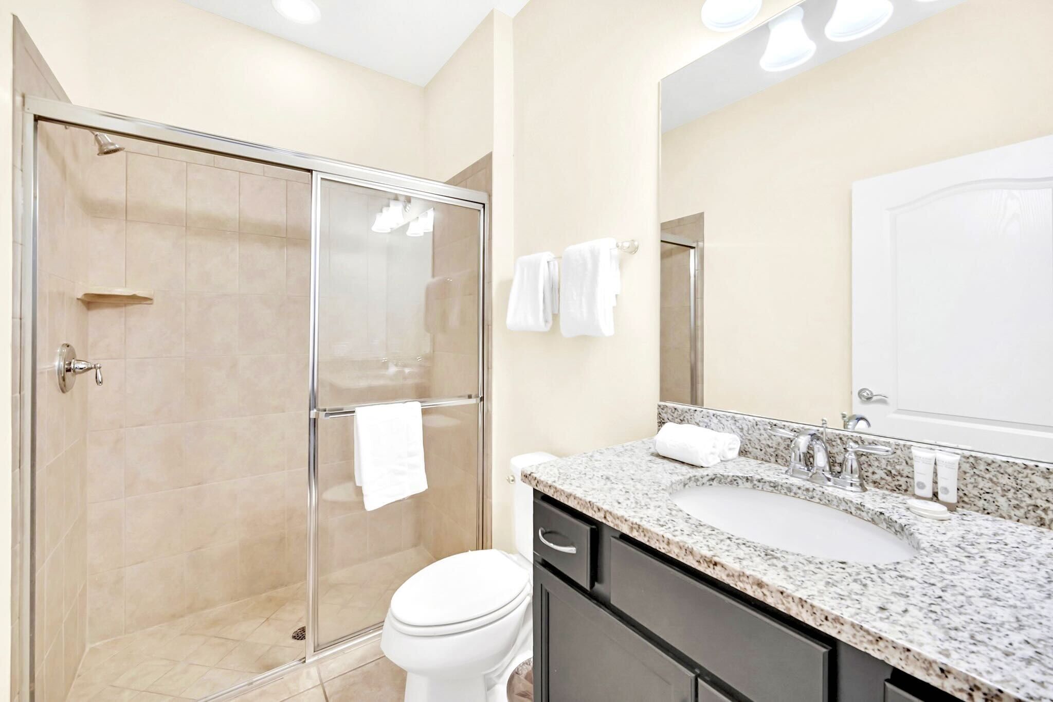 Un bany modern amb dutxa de vidre, un lavabo amb taulell de granit i un vàter.