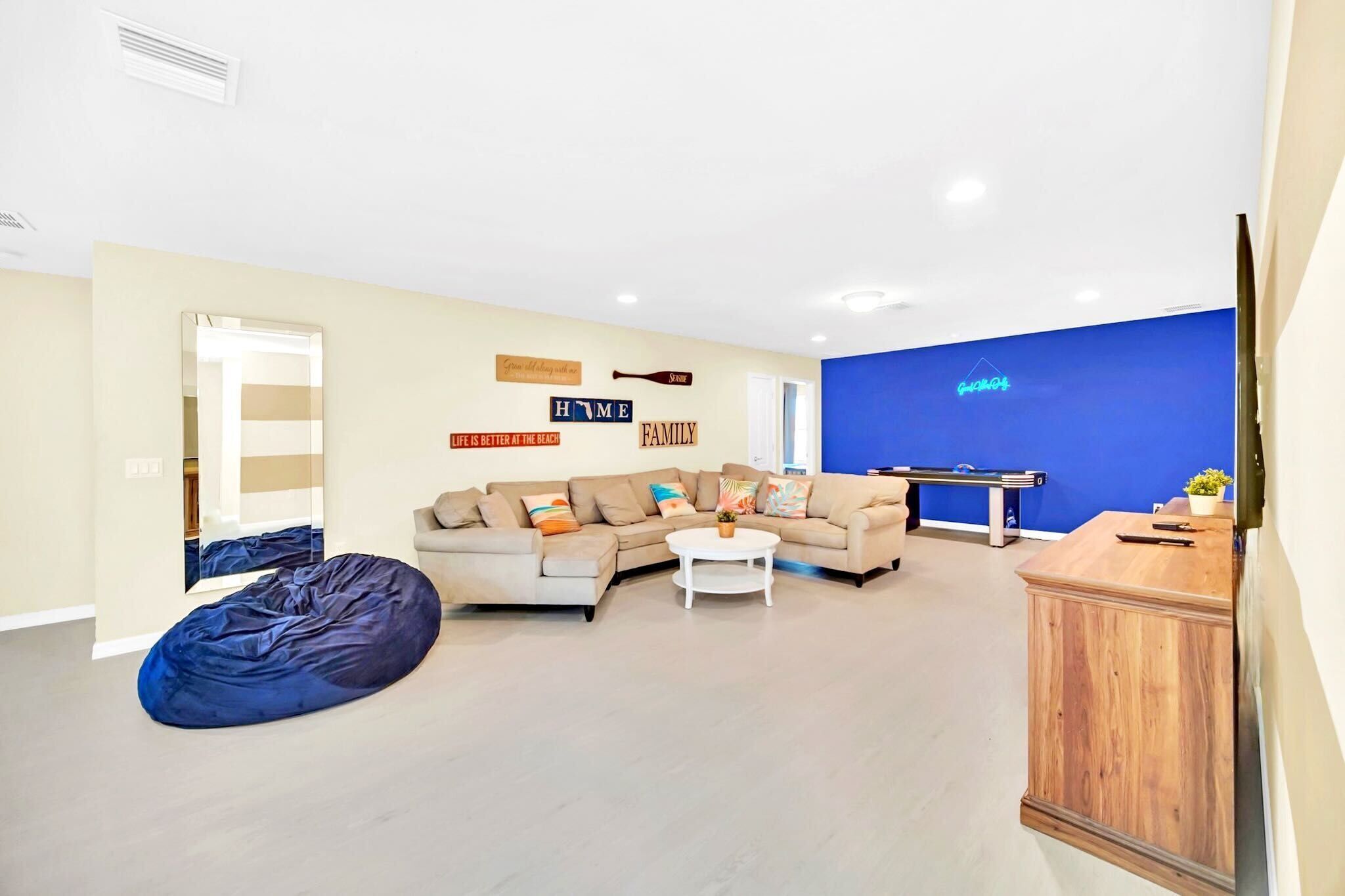 A modern living room with a beige sofa, a blue bean bag, and a white coffee table. There is a blue accent wall and a wooden cabinet.