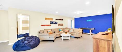 A modern living room with a beige sofa, a blue bean bag, and a white coffee table. There is a blue accent wall and a wooden cabinet.