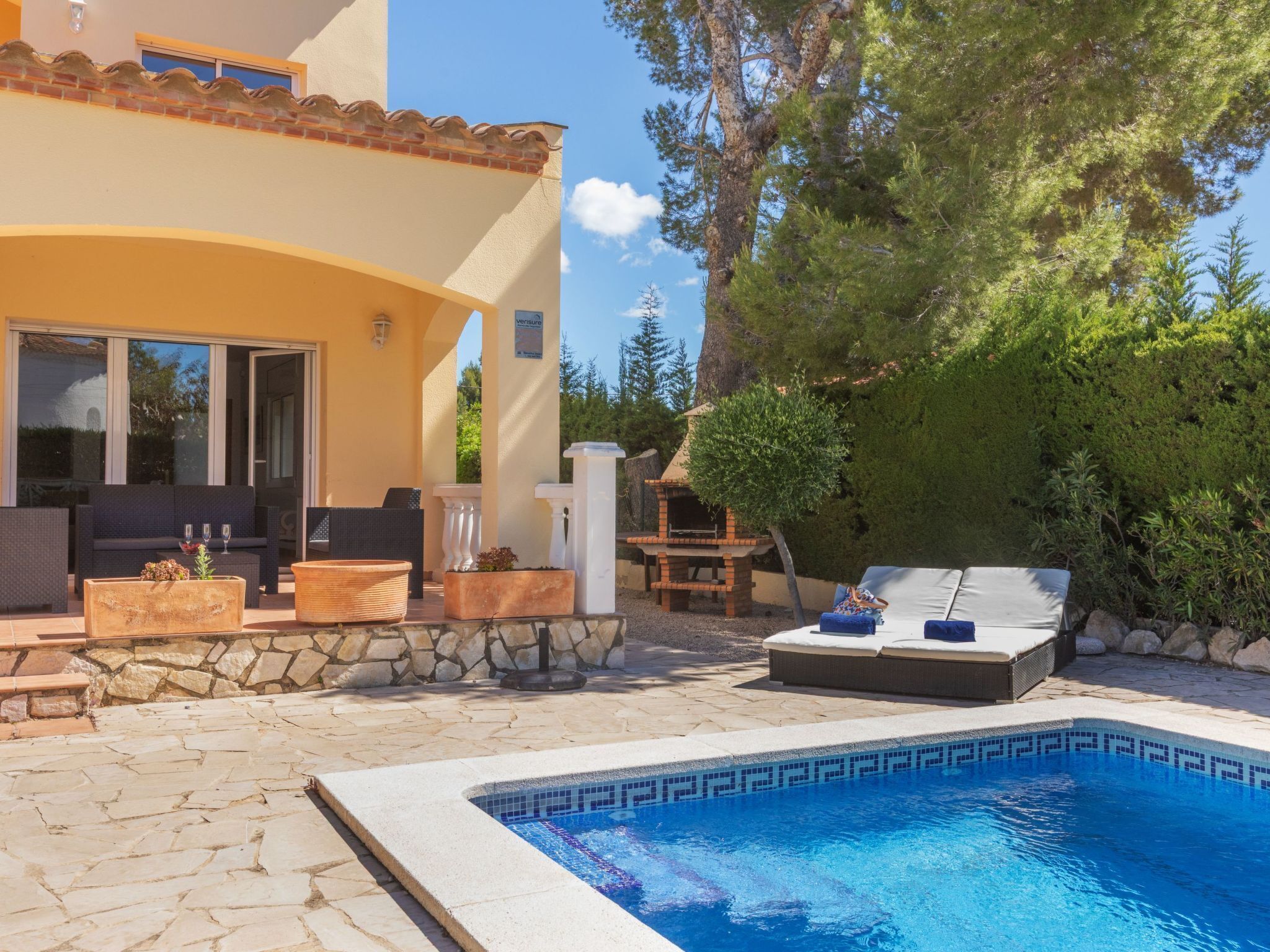 A poolside area with a stone patio, outdoor seating, and a barbecue grill.