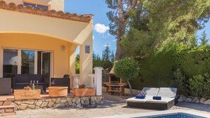Zona de piscina con patio de piedra, mobiliario exterior y una parrilla.