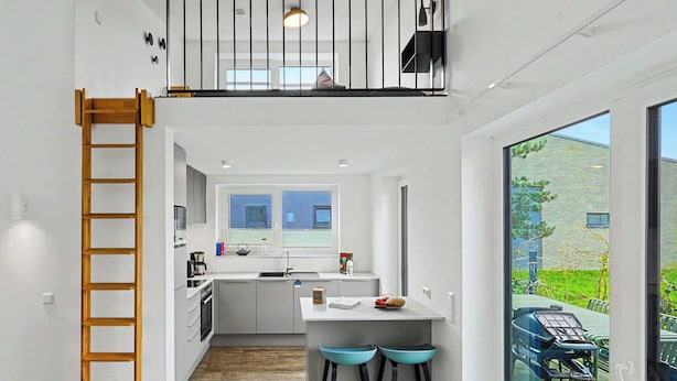 Una cucina moderna con isola centrale, un'area pranzo con due sgabelli, una camera soppalcata con balcone e vista sull'esterno.
