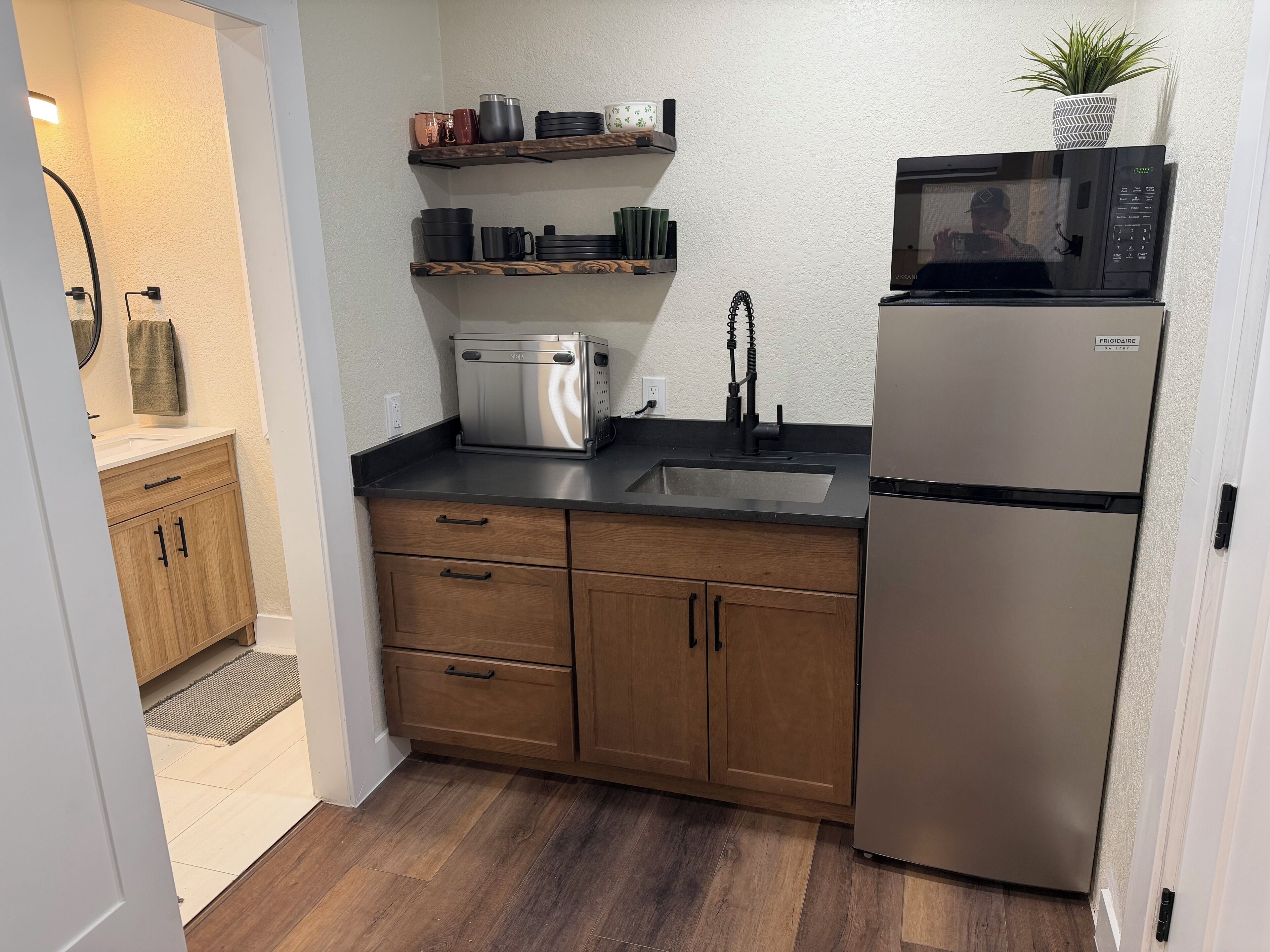 Een kleine keuken met houten kastjes, een roestvrijstalen koelkast, een magnetron en een spoelbak.