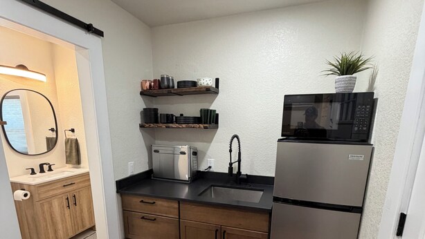 Una cocina compacta con armarios de madera, un refrigerador de acero inoxidable, un microondas y un lavamanos.
