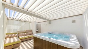 Ett soligt utomhusområde med en bubbelpool, ett trädäck och bekväma sittplatser.