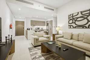 A modern living room with a sofa, coffee table, and a dining area with a kitchen in the background. - Oshima Grande Downtown 1BR Burj Khalifa (Dubai)