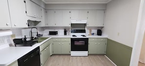 A compact kitchen with white and green cabinets, a microwave, a stove, and a dishwasher.