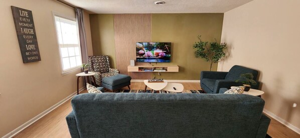 A living room with a large sofa, a TV, a patterned armchair, and a small coffee table.