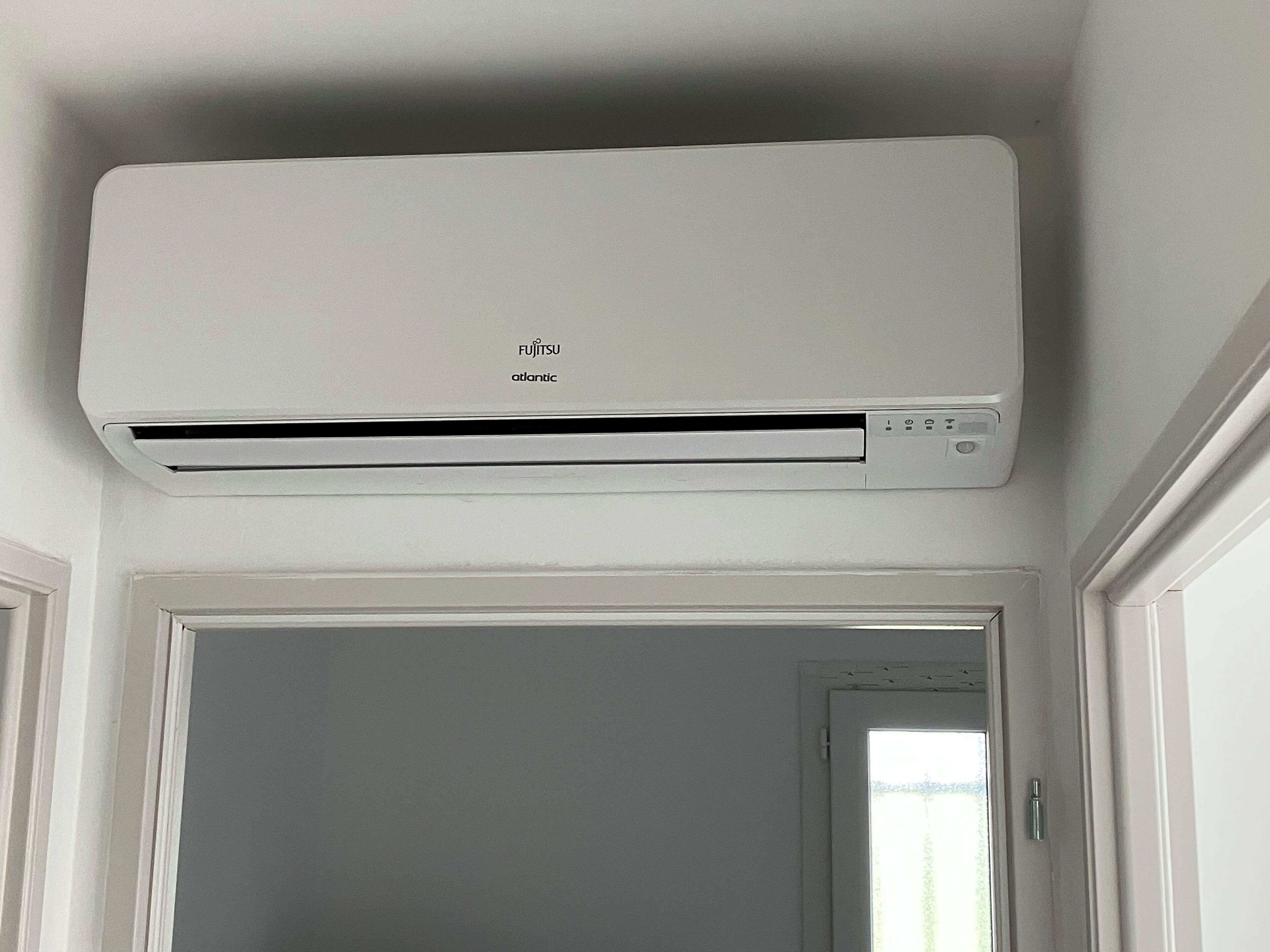 Un appareil de climatisation blanc, fixé au mur dans une pièce dont les moulures sont également blanches.