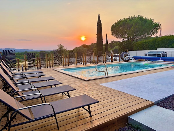 Zona de piscina con sillones reclinables y vistas al atardecer.