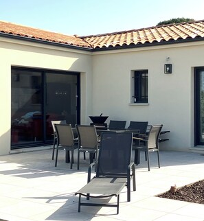 Une terrasse extérieure avec une table et des chaises, une porte-fenêtre coulissante et un toit recouvert de tuiles.