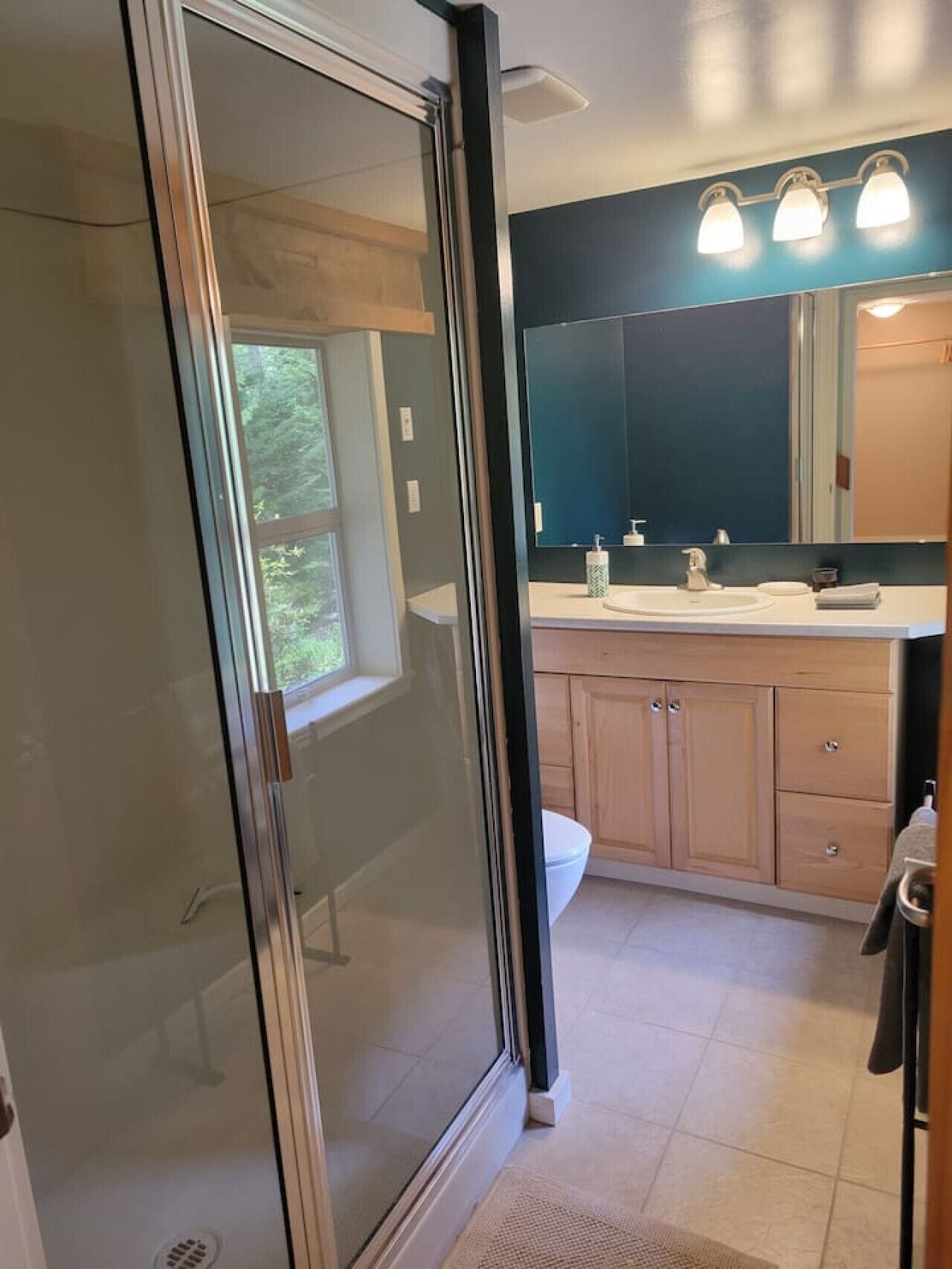 Un bagno moderno con cabina doccia in vetro, uno specchio grande e un mobile lavabo con lavandino e piano di lavoro.