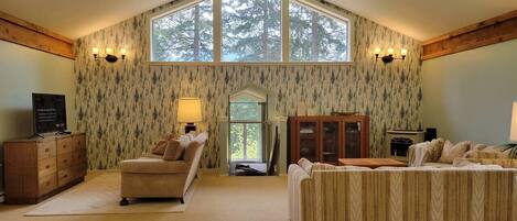 A spacious room with a high ceiling, large windows, a ceiling fan, and two sofas.