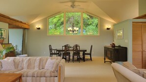 A spacious living room with a high ceiling, a dining table with chairs, a sofa, and a cabinet. - Relaxing 1 bdr + den rainforest retreat with patio (Bowen Island)