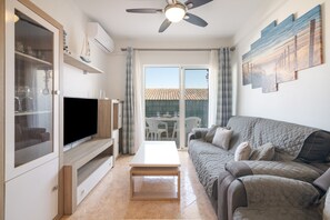 A living room with a flat-screen TV, a sofa, a coffee table, and a ceiling fan. - Cisne del Mar Apartment with Private Terrace, Wi-Fi, and Air Conditioning (Punta Umbría)