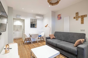 A modern living room with a grey sofa, a white coffee table, and a desk with chairs. There is a sign on the wall that reads "WELCOME TO A RUM". - Charming Renovated Studio - 2P - Cannes Meynadier (Cannes)