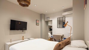 Ein modernes Hotelzimmer mit einem großen Bett, einem Schreibtisch, einem Sessel, einem Fernseher und einer kleinen Küchenzeile.