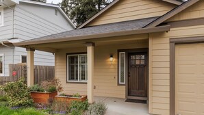 A residential house with a covered porch, a garage, and a front yard with plants.