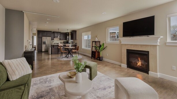 A spacious living room with a fireplace, a television mounted above it, and a kitchen in the background.