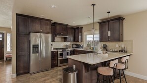 A modern kitchen with dark wood cabinets, stainless steel appliances, a central island with bar stools, and pendant lighting.