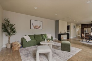 A modern living room with a green sofa, a white coffee table, and a small white stool.