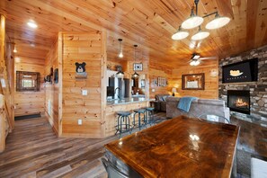 A wooden cabin interior with a bar area, stone fireplace, and a cozy seating area. - Indoor Pool • Game Room • 1 Mile to Strip (Pigeon Forge)