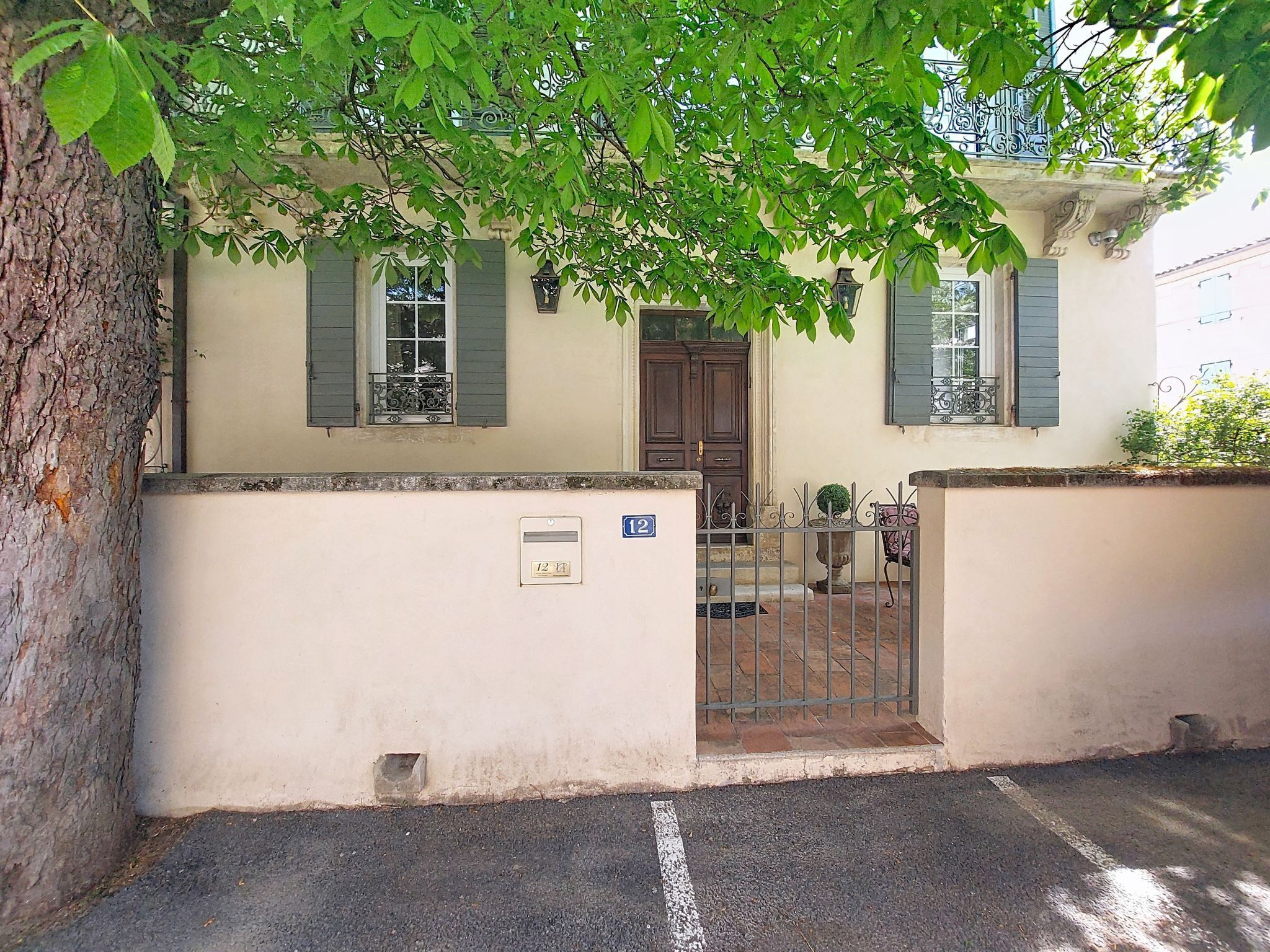 A two-story building with a beige facade, green shutters, and a metal gate.