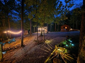 A rustic cabin with a wooden deck, surrounded by trees and a gravel path.