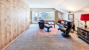 Ein geräumiges Wohnzimmer mit einem großen Holzschrank, einem schwarzen Ledersofa, einer roten Lampe und Blick auf die Stadt durch ein großes Fenster.