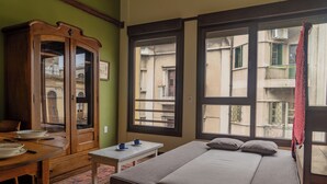 A room with a bed, a wooden cabinet, a small table, and large windows. - Taylor's Port [3] Landing in the Old Town (Montevideo)