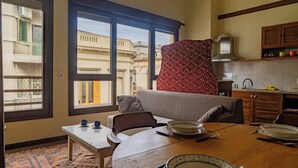A dining area with a table set for four, a sofa, and a view of buildings through large windows. - Taylor's Port [3] Landing in the Old Town (Montevideo)