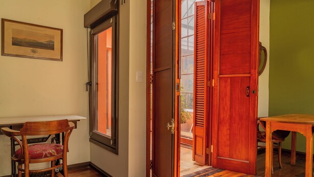 A room with a wooden floor, a table, a chair, and a door leading to an outdoor area. - Taylor's Port [3] Landing in the Old Town (Montevideo)