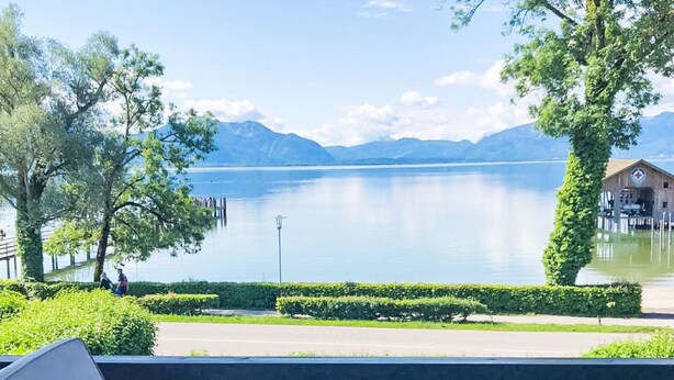 Een terras met een tafel, stoelen en uitzicht op een meer en bergen.