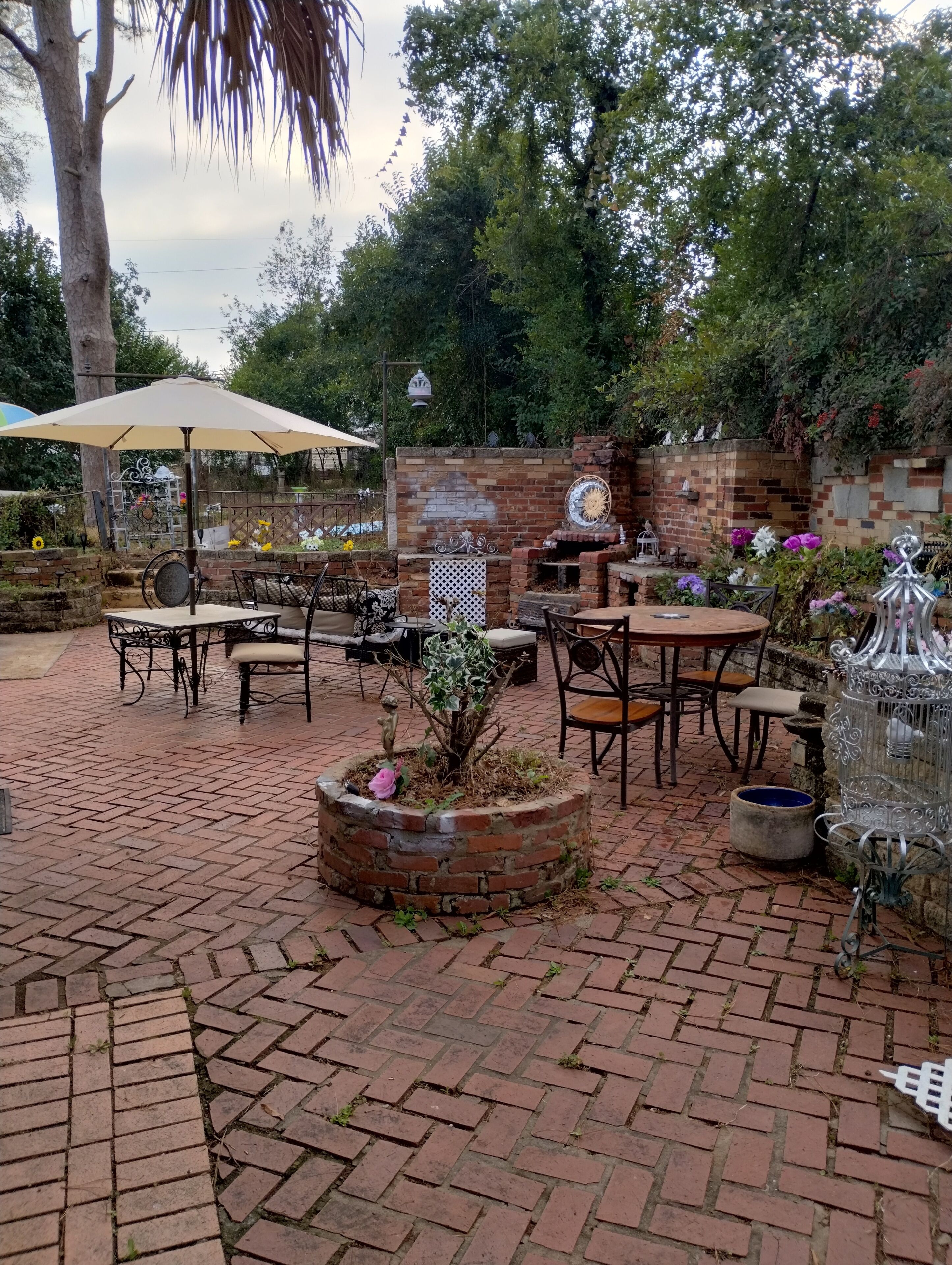 An outdoor patio with brick flooring, multiple tables and chairs, a decorative birdcage, and a brick wall with a decorative metal gate.