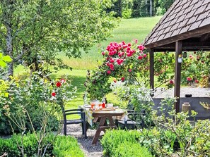 A garden with a table and chairs, surrounded by lush greenery and flowering plants.