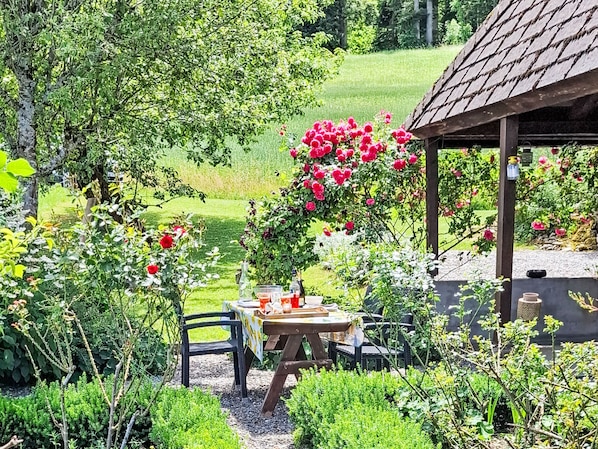 A garden with a table and chairs, surrounded by lush greenery and flowering plants.