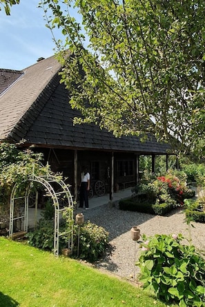 A traditional house with a dark tiled roof, a covered porch, and a garden with various plants and a metal arbor.
