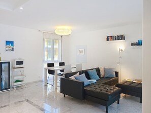 A modern living room with a black leather sofa, a glass coffee table, and a dining area with a white table and chairs. - Apt. Hermosa by Interhome (Locarno)