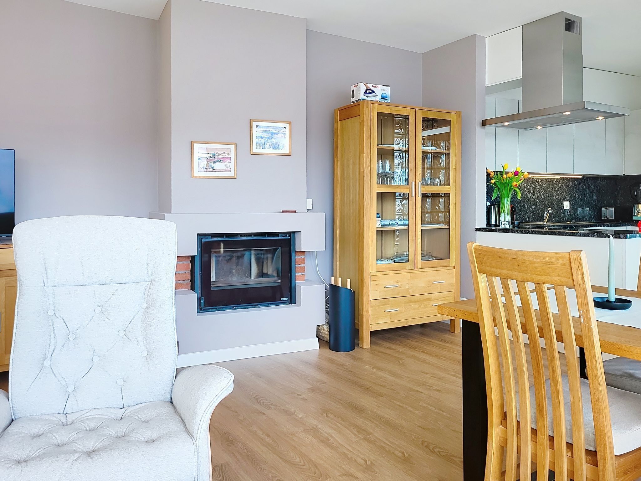 Ein modernes Wohnzimmer mit Kamin, einer Holztruhe mit Glastüren und einem Essbereich mit einem hölzernen Stuhl.
