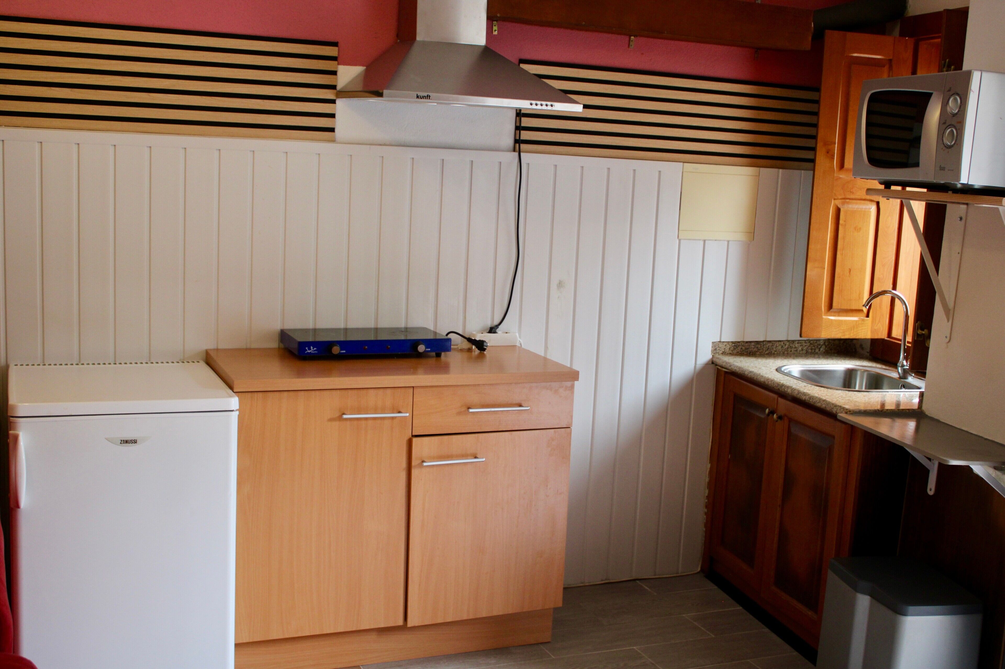 Una cocina compacta con microondas integrado, un refrigerador pequeño, armarios de madera y una encimera.
