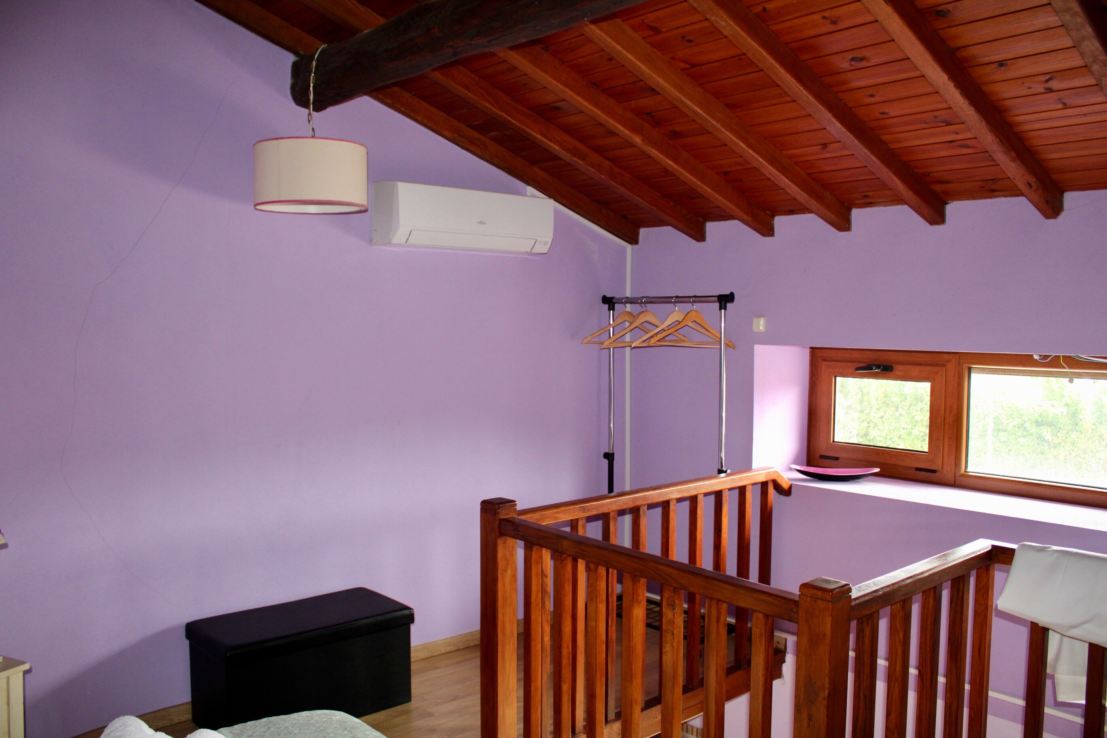 Une pièce avec un plafond en bois, une lampe suspendue, une fenêtre donnant sur un beau paysage, un étendoir et une boîte de rangement noire.
