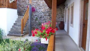 Edifici de pedra amb una escala de fusta, una caixa de flors amb flors vermelles i roses, i un passadís amb portes de fusta.