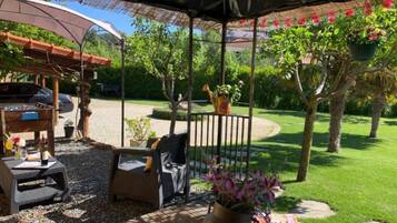 Un patio al aire libre con zona de estar cubierta, una parrilla y vistas a un jardín.