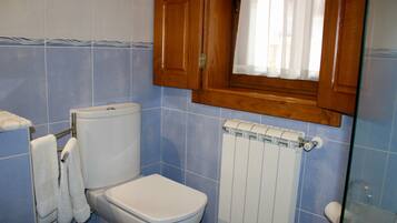 A bathroom with a toilet, a towel rack with towels, a wooden cabinet, and a window with a curtain.