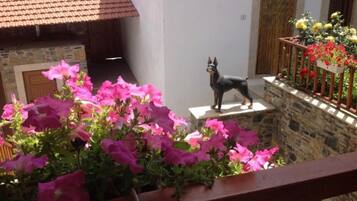 Un balcón con una estatua de perro, flores rosadas y un muro de piedra.