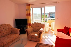 A living room with two patterned sofas, a red sofa, a television, and a sliding glass door leading to an outdoor area.