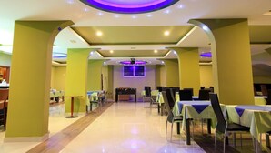 Un grand espace intérieur aménagé avec des tables et des chaises pour les repas, un baby-foot et un plafond agrémenté d’un luminaire décoratif.